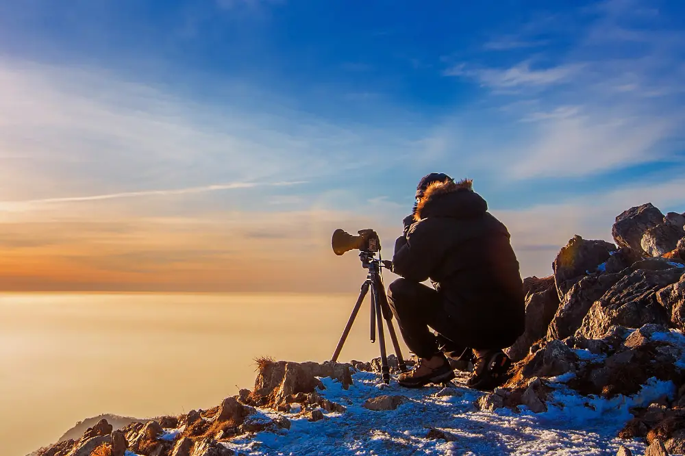 photographe en montagne sur la neige au dessus des nuages